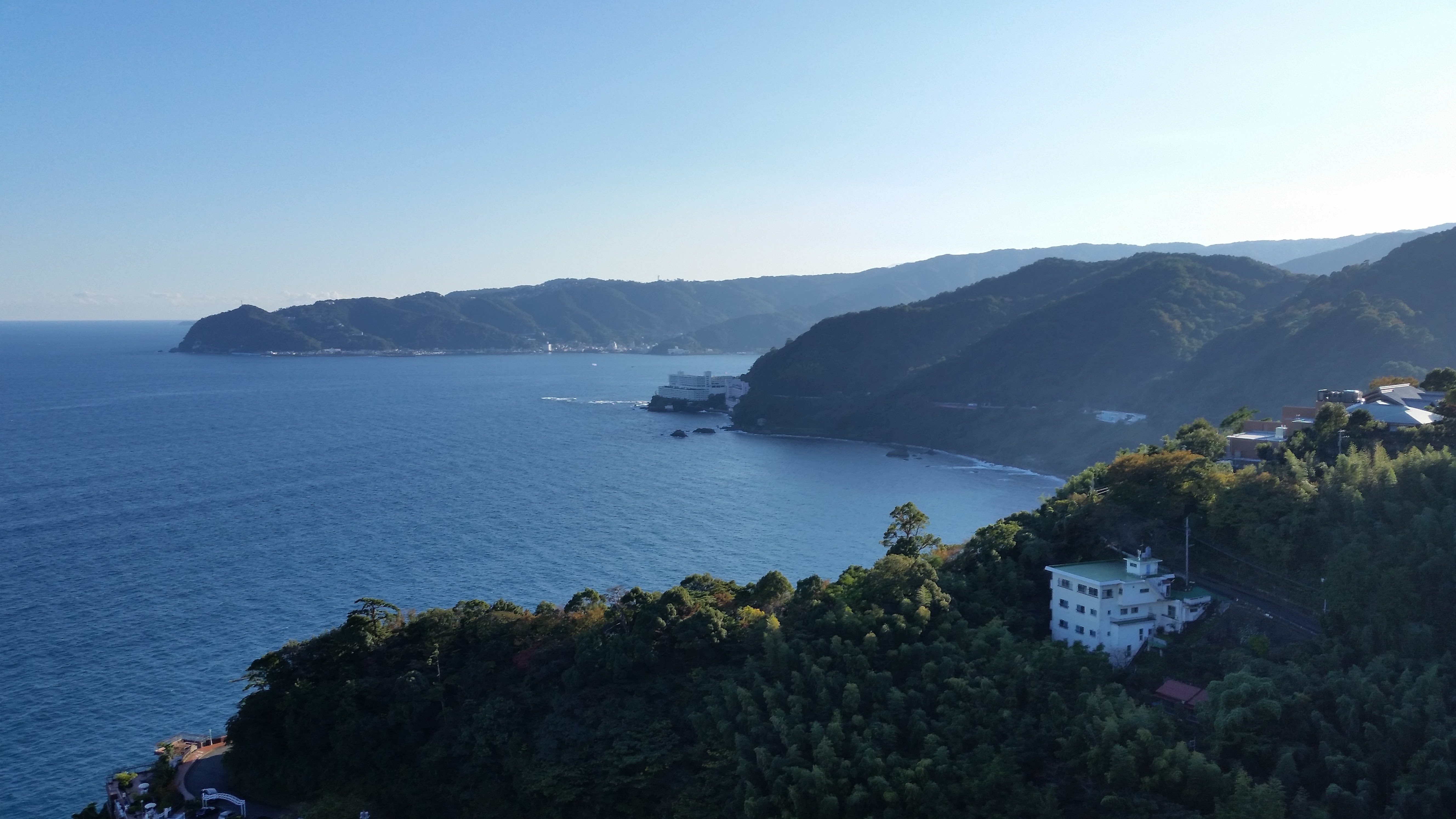 View of the Izu coast from the heights above Atami: vegetation-covered cliffs, deep blue sea and hotels perched at the water's edge