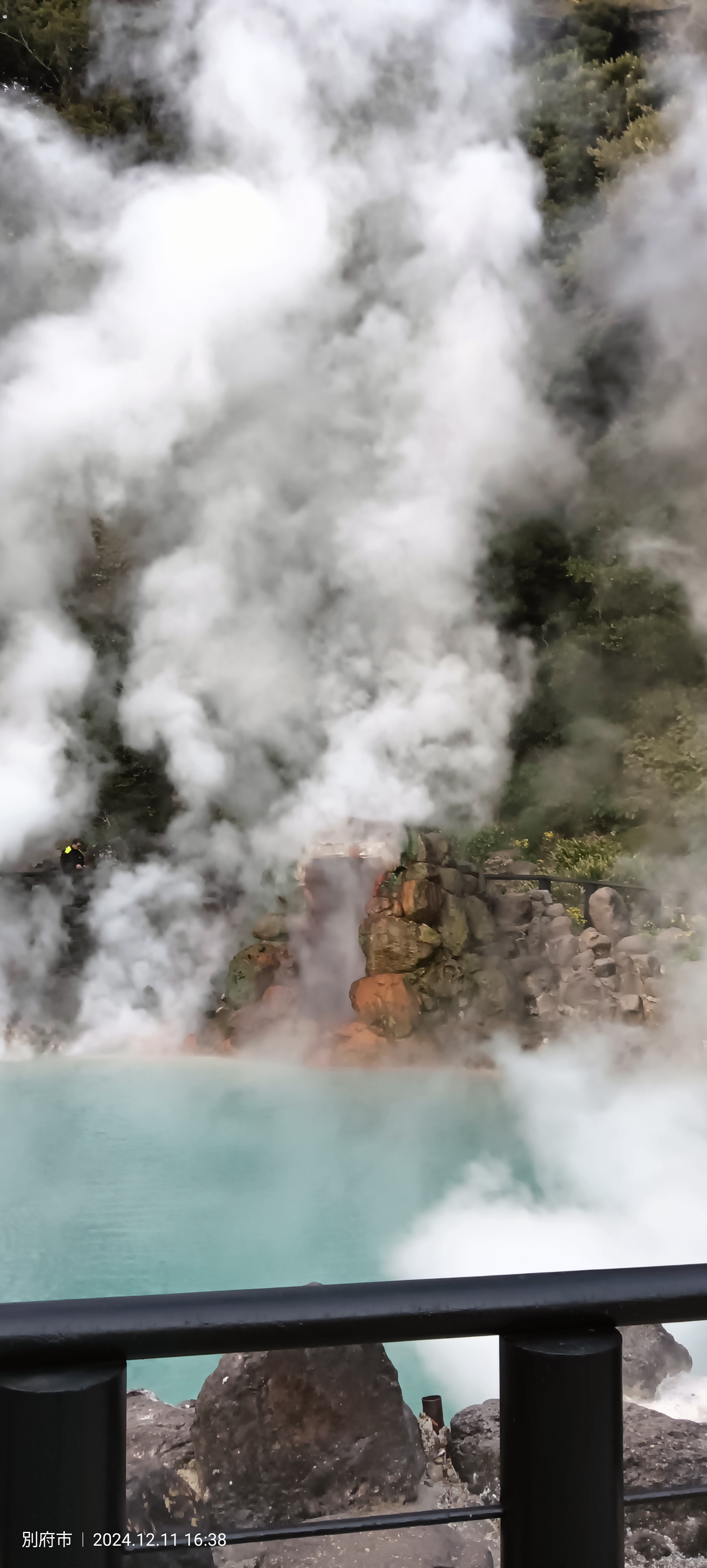 Massive white steam column rising from Umi Jigoku above the turquoise thermal water, with orange mineral deposits visible on the rocks below
