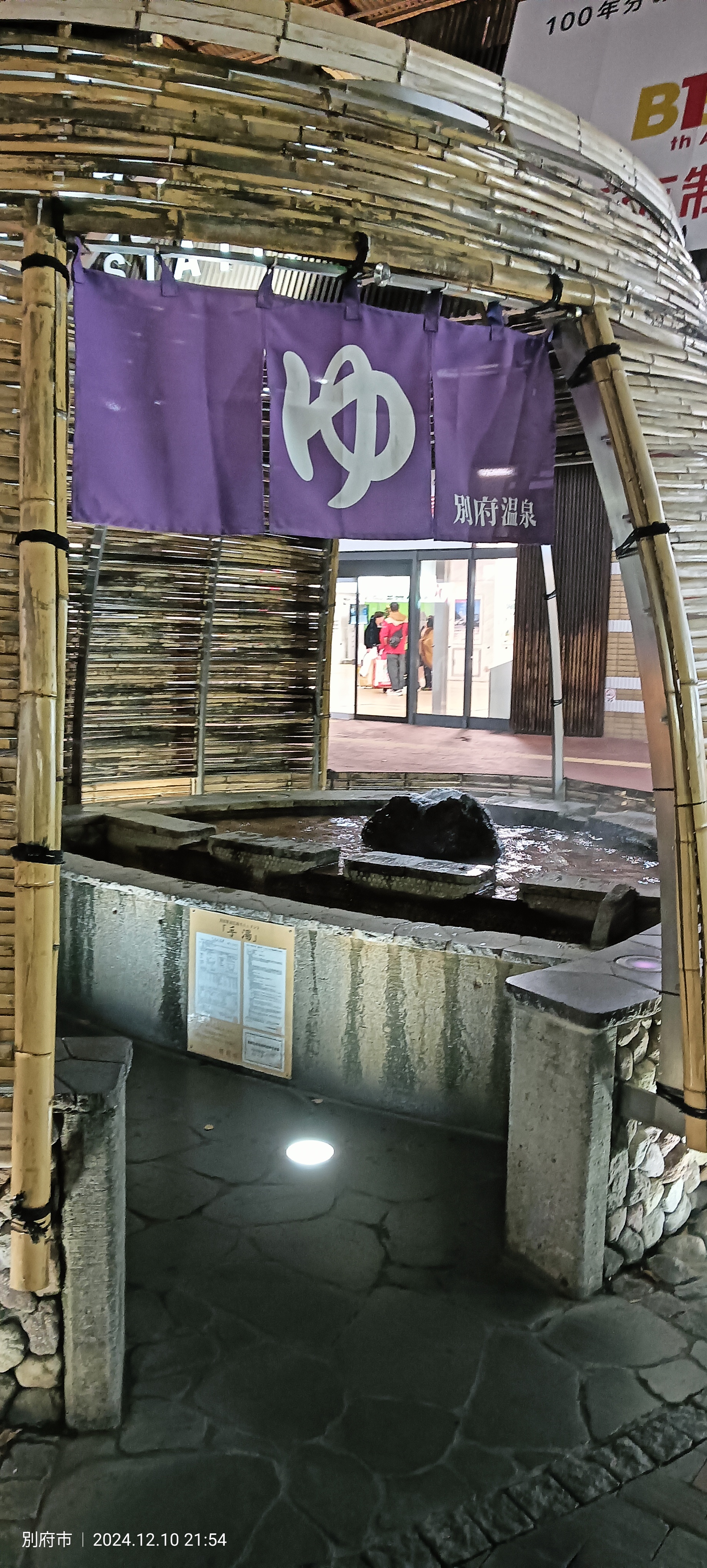 Public foot bath (ashiyu) outside Beppu station with a purple noren bearing the kanji "ゆ" and a Beppu Onsen sign