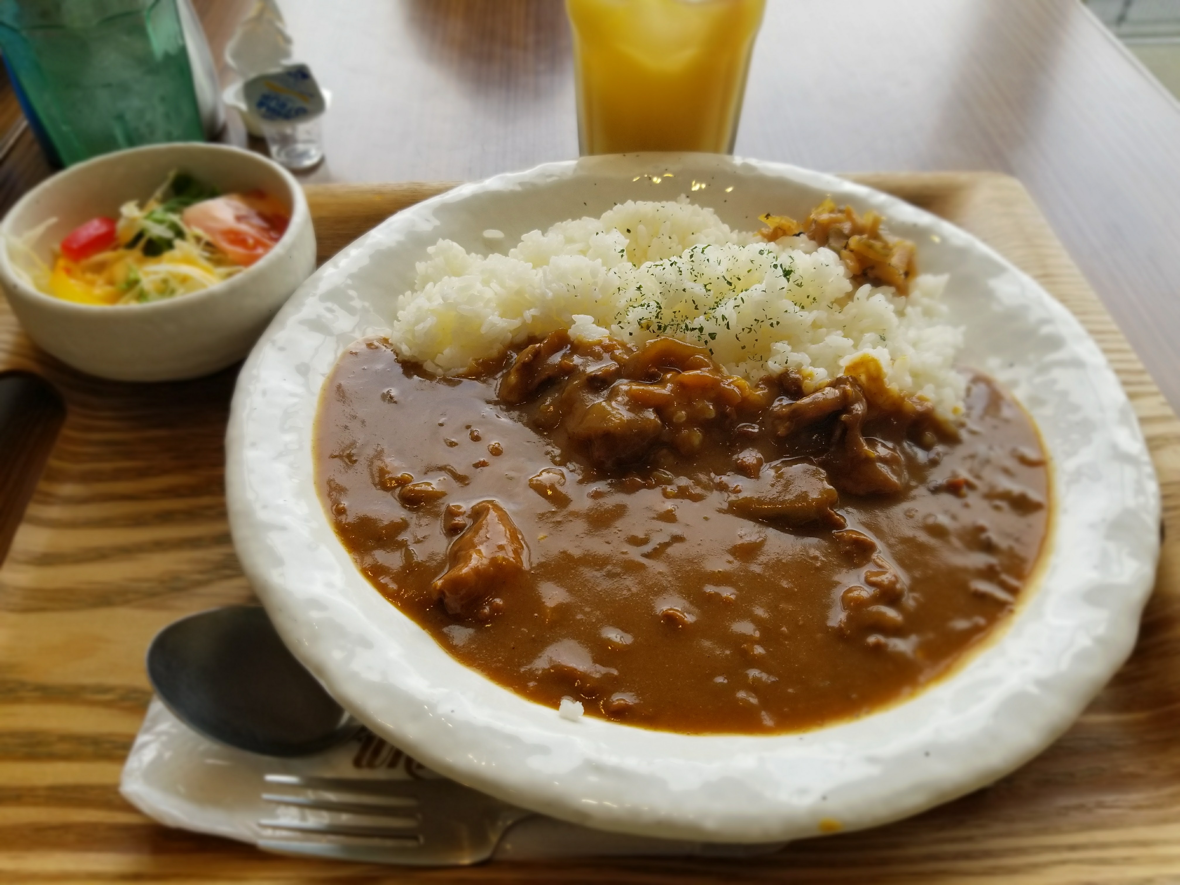 Japanese curry in a rustic white bowl at a sit-down restaurant, with a side salad