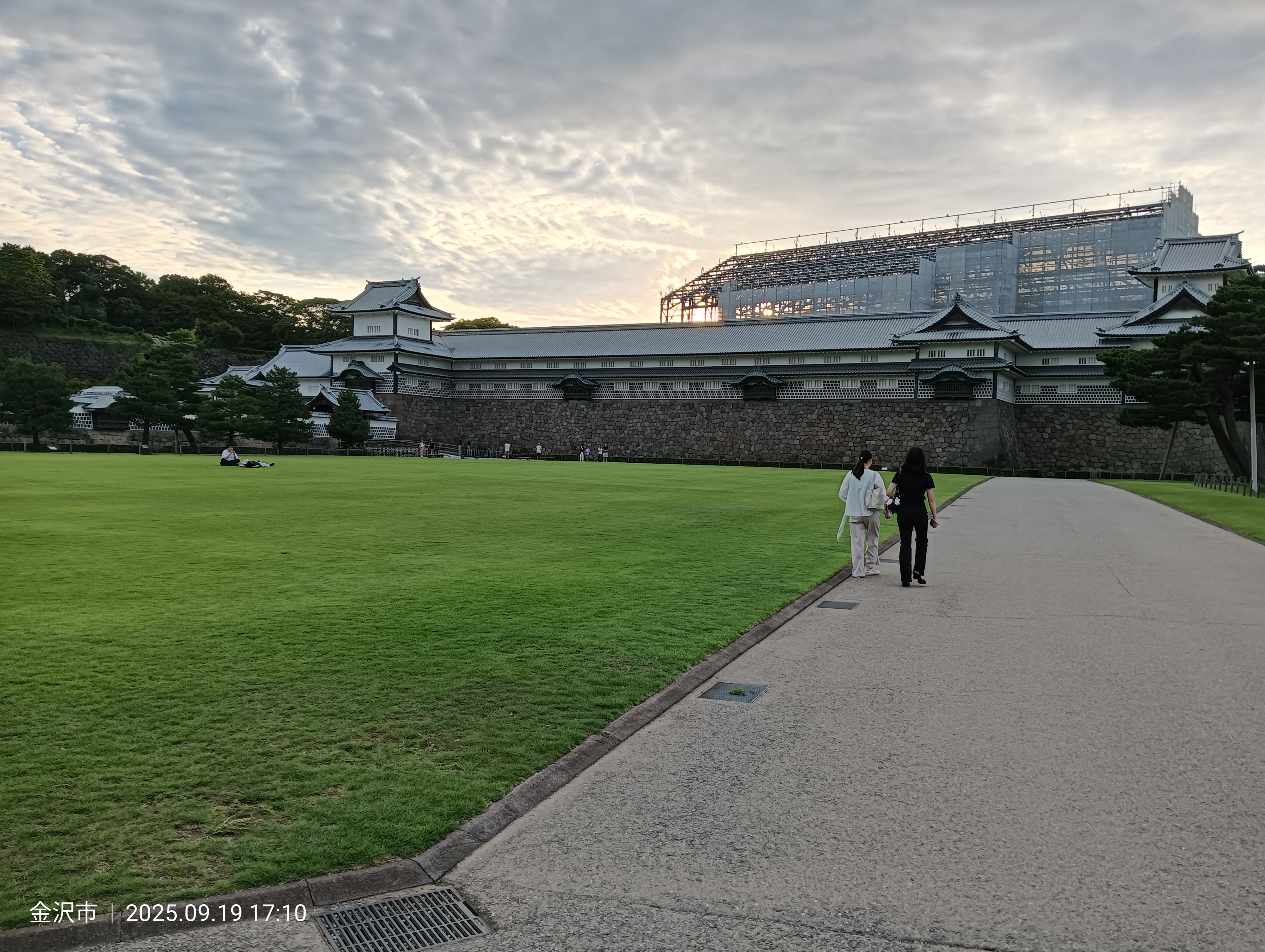 El recinto interior del castillo de Kanazawa al atardecer, con visitantes en kimono paseando por el césped