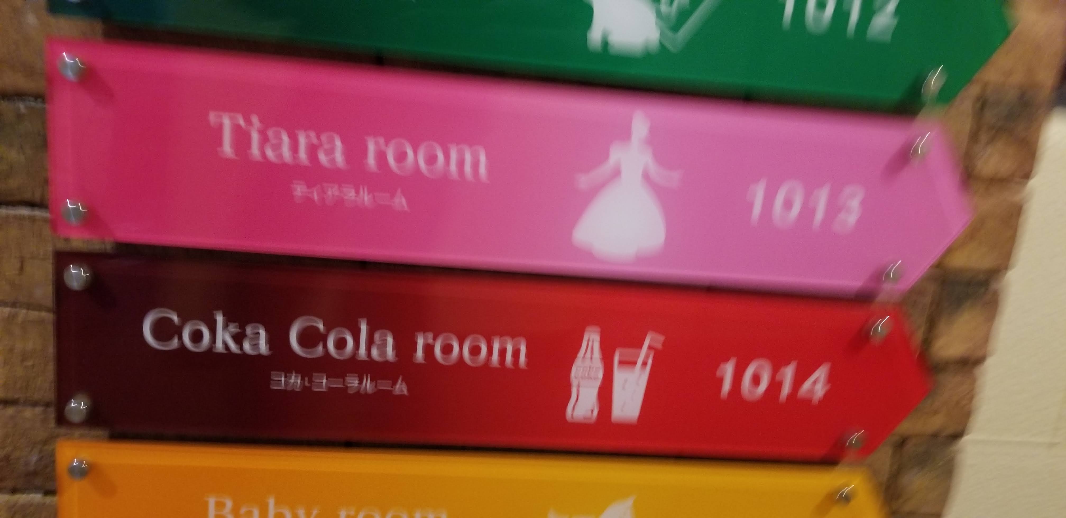 Themed room signs in the hotel corridor: Tiara room (pink, with a princess silhouette), Coka Cola room (red) and Baby room (yellow)
