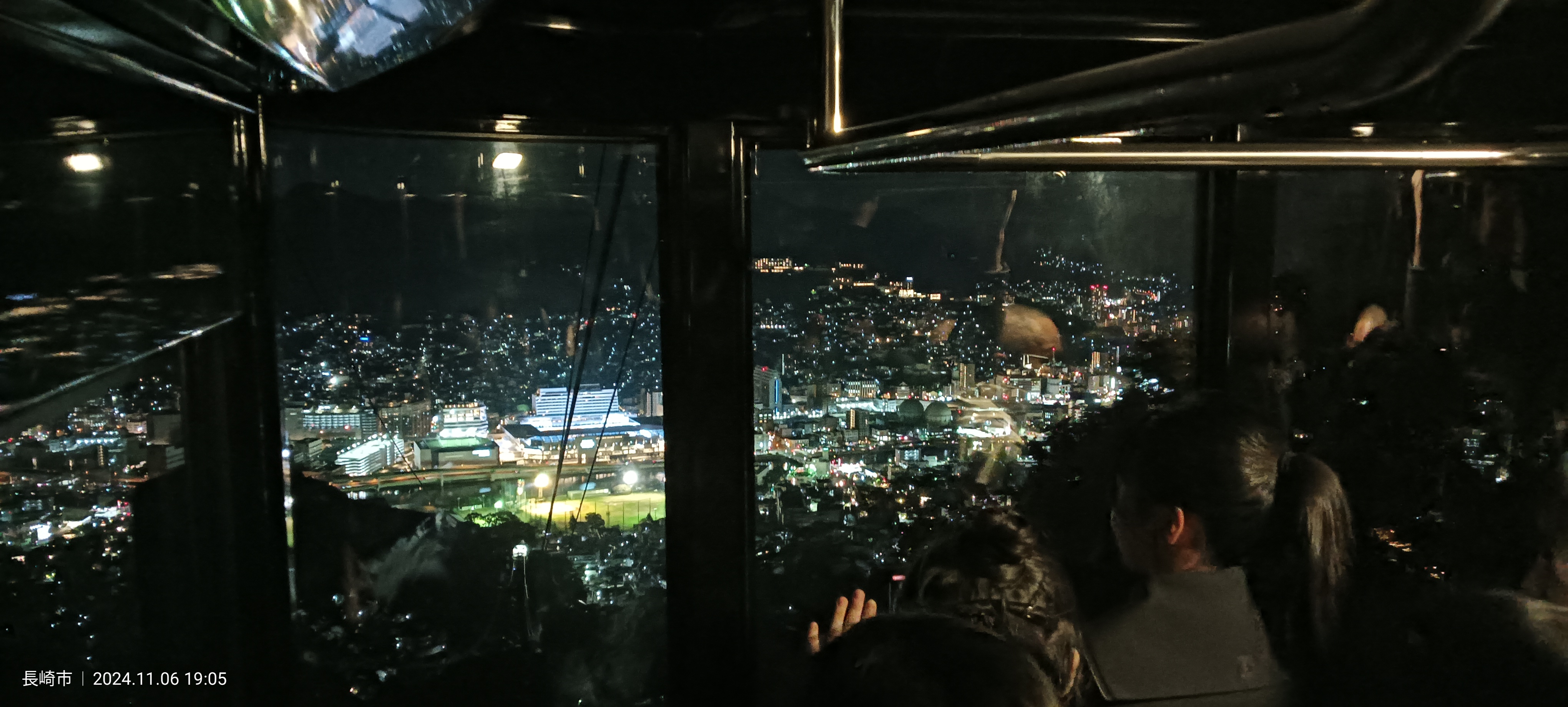 Interior del teleférico del Monte Inasa de noche, con los pasajeros mirando por las ventanas hacia las luces de la ciudad durante el ascenso