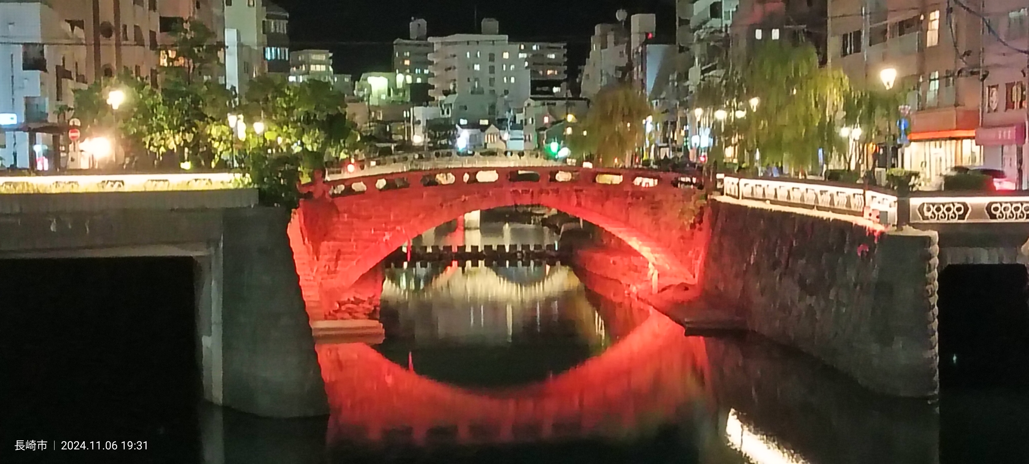 El Puente Meganebashi (眼鏡橋) de Nagasaki iluminado en rojo de noche, con su reflejo en el río formando la figura de unas gafas